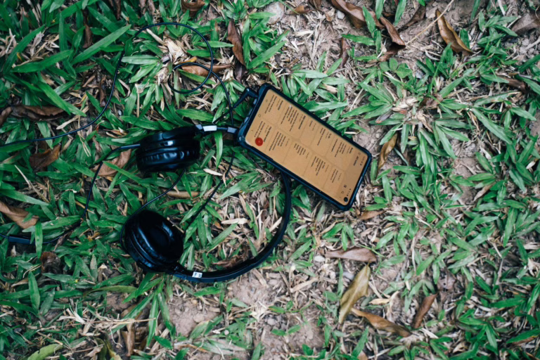 Close-up of black headphones and smartphone placed on green grass outdoors.